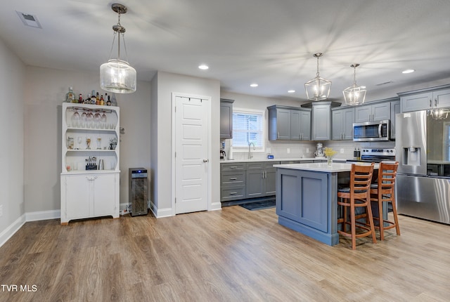 kitchen with light hardwood / wood-style floors, a kitchen island, pendant lighting, and stainless steel appliances