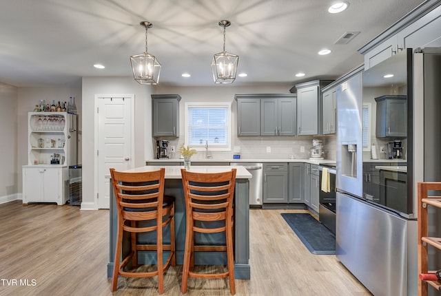 kitchen with light hardwood / wood-style floors, appliances with stainless steel finishes, hanging light fixtures, and a breakfast bar area