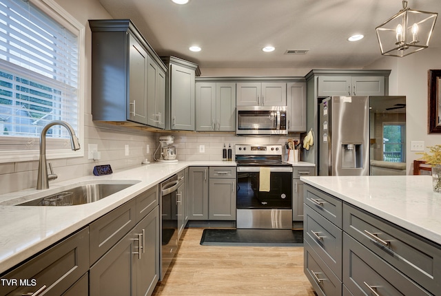 kitchen featuring light stone counters, sink, gray cabinetry, light hardwood / wood-style flooring, and appliances with stainless steel finishes