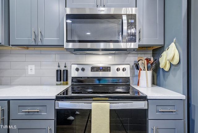 kitchen featuring appliances with stainless steel finishes, gray cabinetry, light stone countertops, and tasteful backsplash