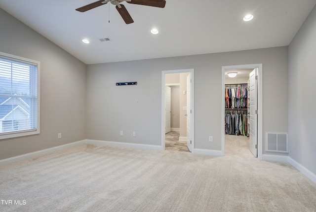 unfurnished bedroom featuring light carpet, ceiling fan, a walk in closet, and a closet