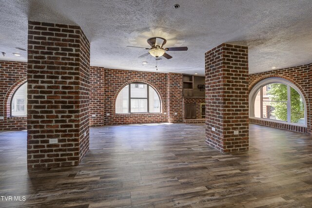 unfurnished living room featuring a wealth of natural light, brick wall, ceiling fan, and dark hardwood / wood-style floors