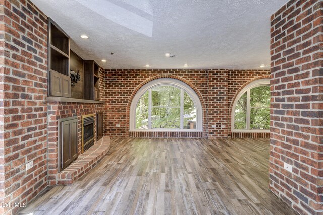 unfurnished living room with a fireplace, a textured ceiling, brick wall, and light hardwood / wood-style floors