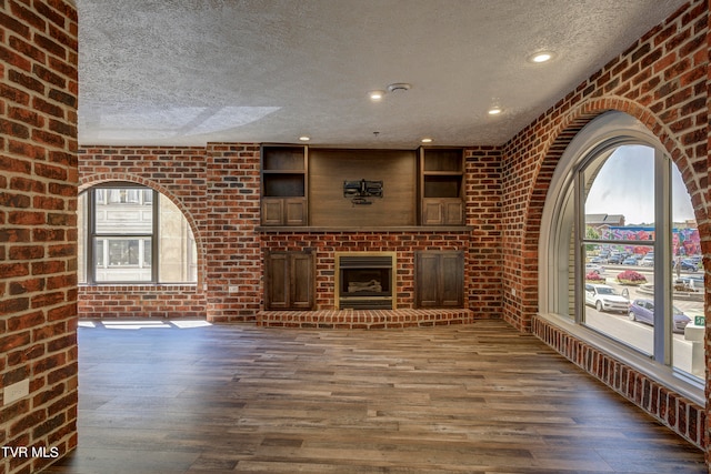 unfurnished living room featuring a fireplace, brick wall, and a textured ceiling