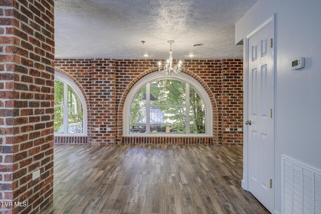 unfurnished dining area featuring a textured ceiling, dark hardwood / wood-style flooring, and brick wall