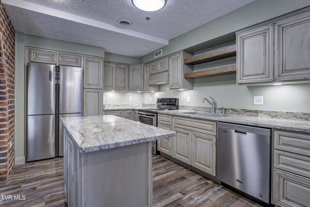 kitchen featuring a textured ceiling, stainless steel appliances, a center island, sink, and dark wood-type flooring