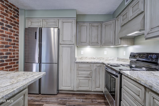 kitchen featuring appliances with stainless steel finishes, light stone counters, custom exhaust hood, dark hardwood / wood-style floors, and a textured ceiling