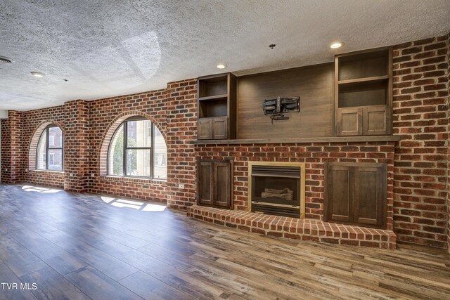 unfurnished living room with a textured ceiling, brick wall, wood-type flooring, and a fireplace