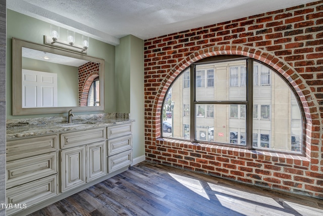 bathroom with vanity, a textured ceiling, hardwood / wood-style flooring, and brick wall