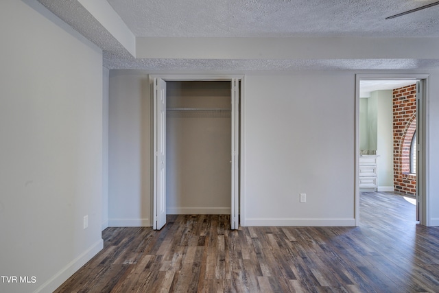 unfurnished bedroom with dark wood-type flooring, a closet, brick wall, and a textured ceiling