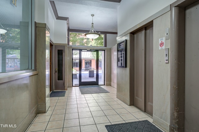 tiled foyer with elevator, a textured ceiling, and ornamental molding