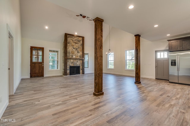 unfurnished living room featuring light wood-type flooring, a healthy amount of sunlight, and a stone fireplace