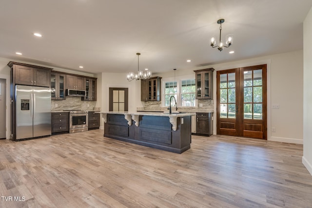 kitchen featuring appliances with stainless steel finishes, dark brown cabinets, light hardwood / wood-style floors, and hanging light fixtures