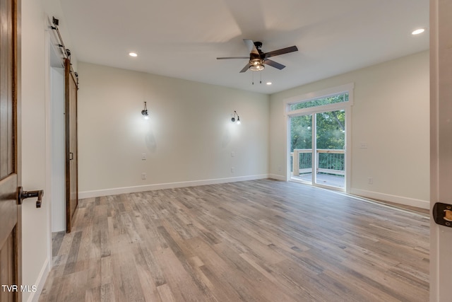 empty room with a barn door, ceiling fan, and light wood-type flooring