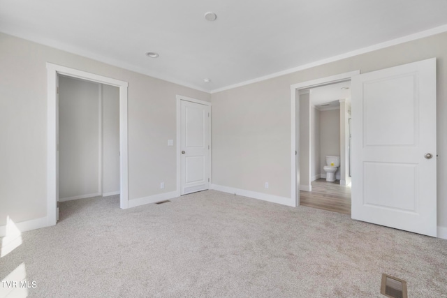 unfurnished bedroom with a closet, light colored carpet, connected bathroom, and crown molding