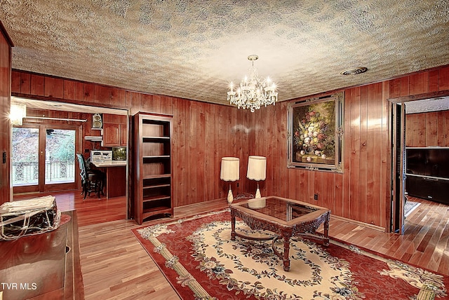 sitting room with a notable chandelier, wood walls, a textured ceiling, and light hardwood / wood-style flooring