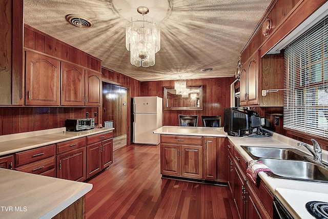 kitchen featuring wood walls, sink, white fridge, and decorative light fixtures