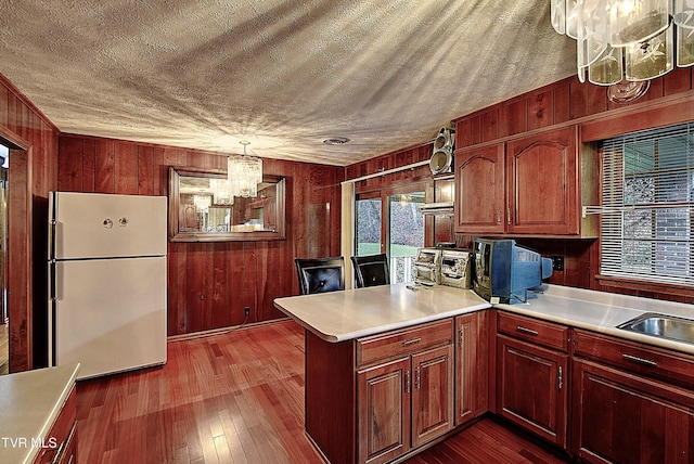 kitchen with dark hardwood / wood-style flooring, wooden walls, white refrigerator, an inviting chandelier, and hanging light fixtures