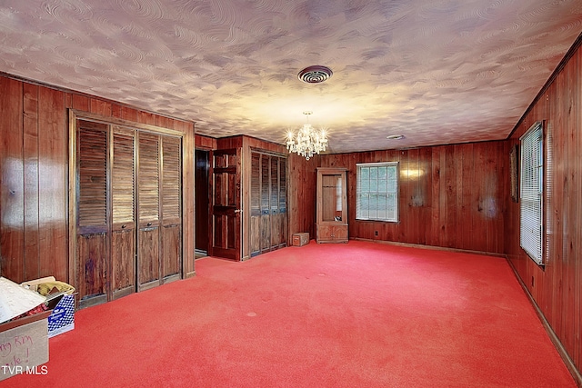 interior space with wood walls, carpet floors, a textured ceiling, and a chandelier