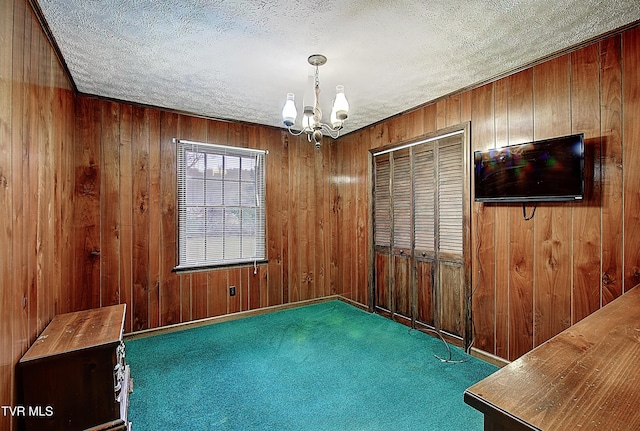 unfurnished room with dark carpet, a textured ceiling, wooden walls, and an inviting chandelier