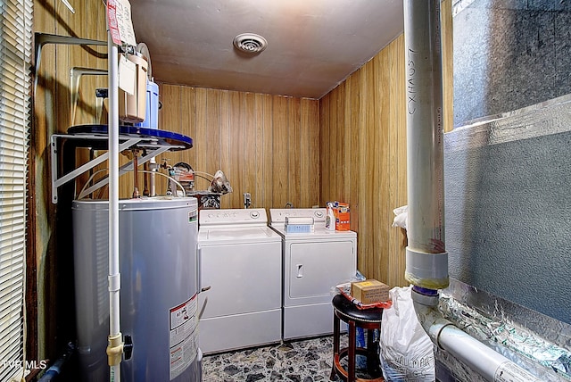 washroom featuring water heater, wooden walls, and washer and dryer