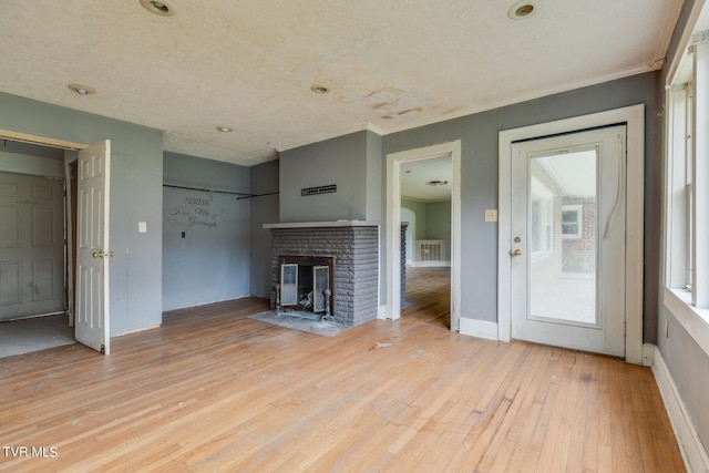 unfurnished living room featuring ornamental molding, a brick fireplace, a textured ceiling, and light hardwood / wood-style flooring