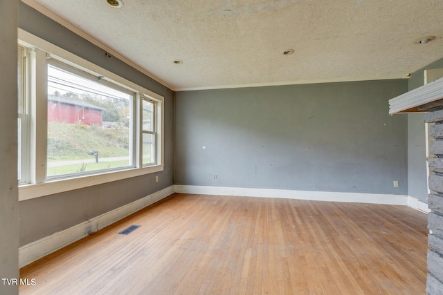 empty room with crown molding, light wood-type flooring, and a textured ceiling