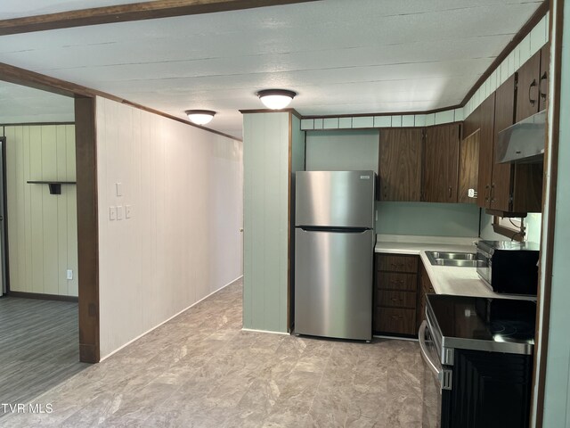 kitchen featuring range, wood walls, stainless steel fridge, and dark brown cabinetry