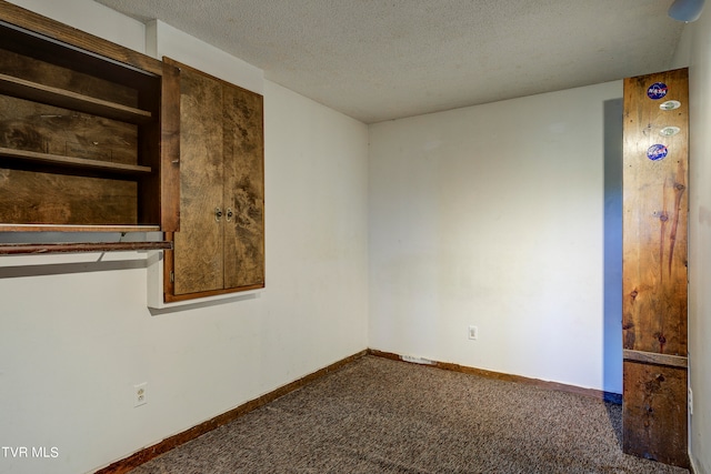 spare room featuring a textured ceiling and dark carpet