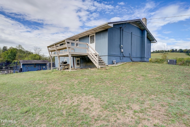 rear view of property featuring cooling unit, an outdoor structure, a wooden deck, and a lawn