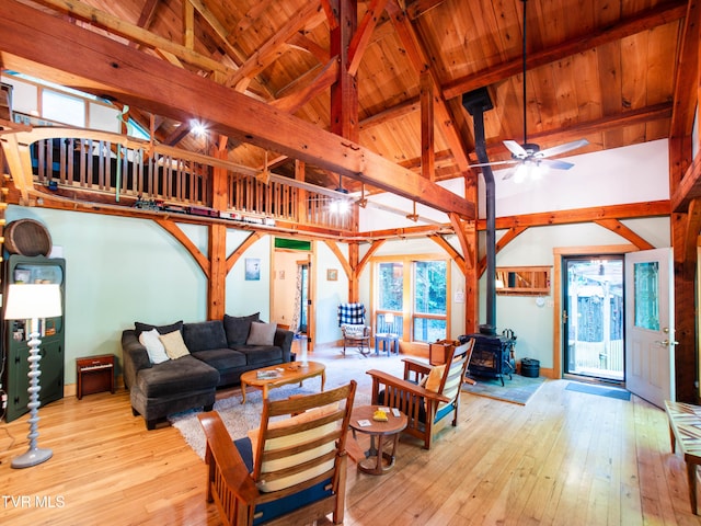 living room featuring ceiling fan, light wood-type flooring, a wood stove, and high vaulted ceiling