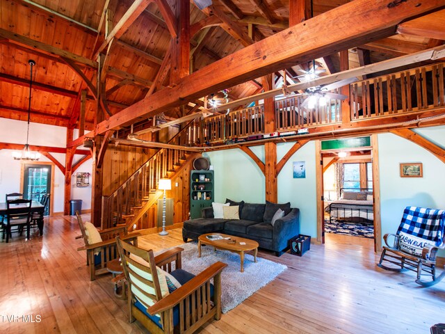 living room with wood ceiling, light wood-type flooring, ceiling fan with notable chandelier, beam ceiling, and high vaulted ceiling