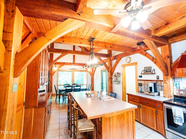 kitchen featuring stainless steel range with electric stovetop, light tile patterned floors, ceiling fan, decorative light fixtures, and a kitchen island with sink