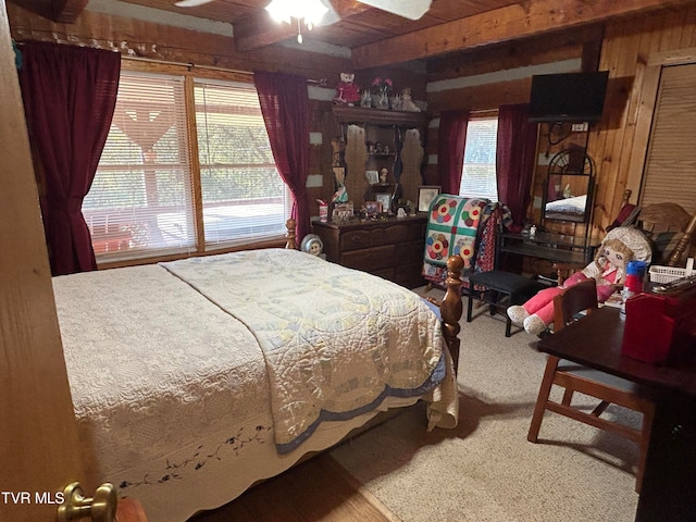 bedroom featuring beamed ceiling, ceiling fan, wooden walls, and carpet flooring