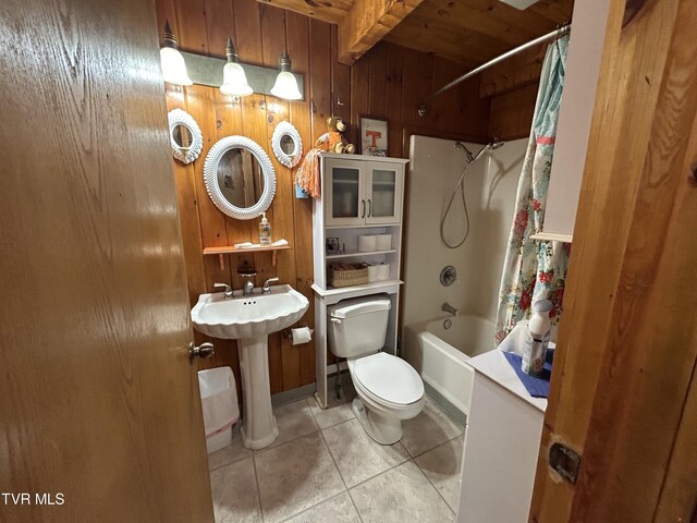 full bathroom featuring tile patterned floors, wooden walls, toilet, beamed ceiling, and shower / bath combo with shower curtain