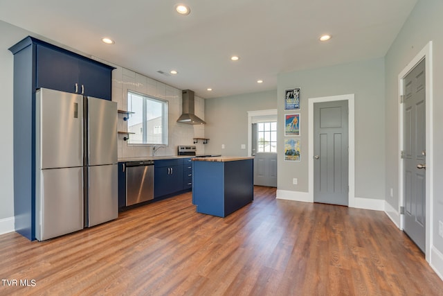 kitchen with a kitchen island, wall chimney range hood, stainless steel appliances, dark hardwood / wood-style flooring, and blue cabinets