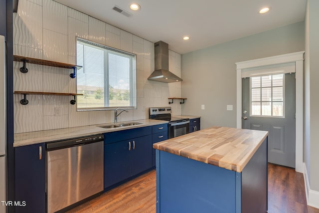 kitchen with appliances with stainless steel finishes, wall chimney exhaust hood, sink, and blue cabinetry