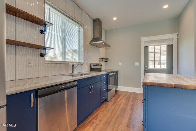 kitchen featuring appliances with stainless steel finishes, wall chimney exhaust hood, blue cabinets, and plenty of natural light