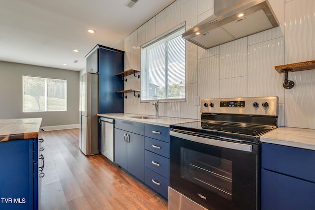 kitchen with exhaust hood, blue cabinets, light hardwood / wood-style floors, and appliances with stainless steel finishes