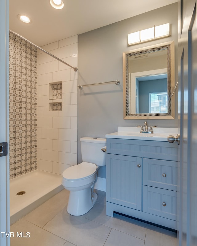 bathroom with tile patterned flooring, tiled shower, vanity, and toilet