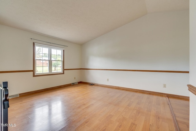 spare room featuring a textured ceiling, light hardwood / wood-style floors, and vaulted ceiling