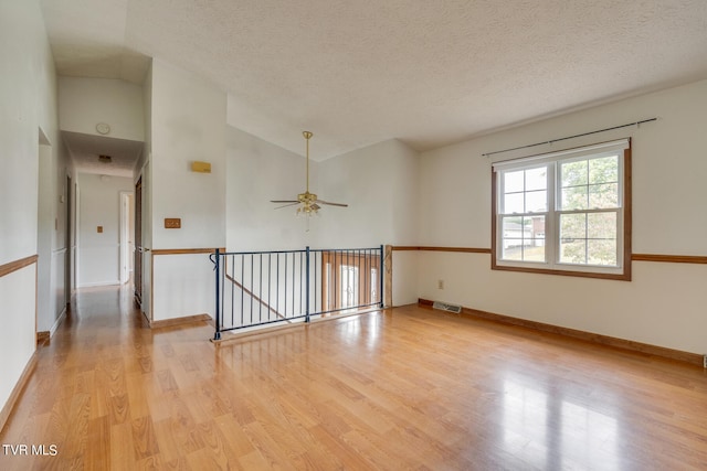 spare room with a textured ceiling, vaulted ceiling, ceiling fan, and light hardwood / wood-style flooring