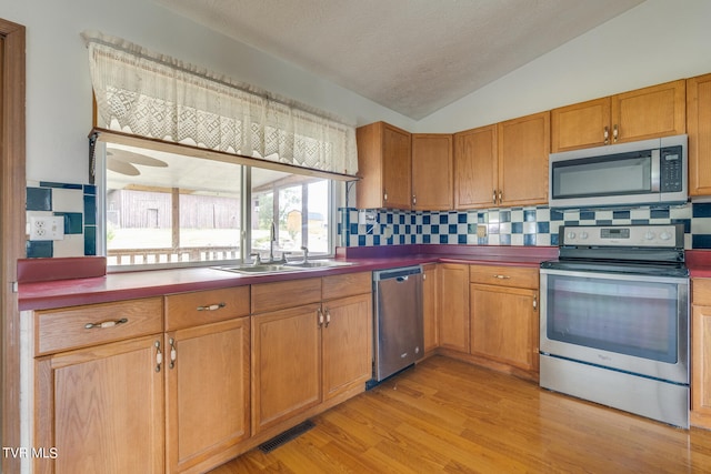 kitchen with light hardwood / wood-style floors, sink, stainless steel appliances, vaulted ceiling, and decorative backsplash