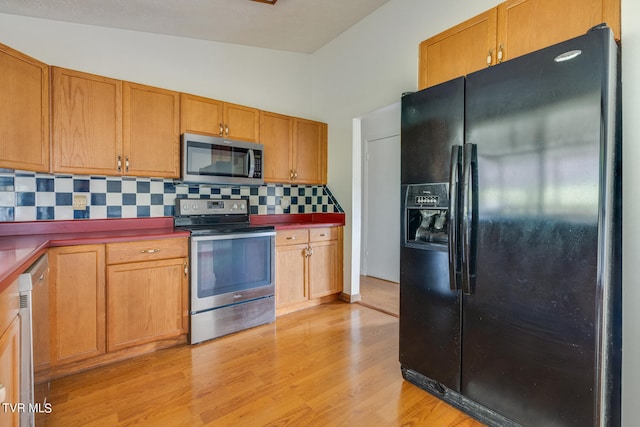 kitchen featuring appliances with stainless steel finishes, decorative backsplash, lofted ceiling, and light hardwood / wood-style flooring