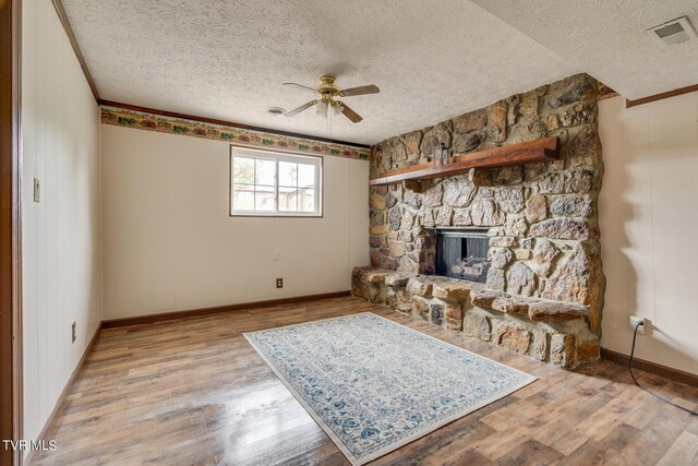 living room with light hardwood / wood-style floors, a textured ceiling, a fireplace, crown molding, and ceiling fan