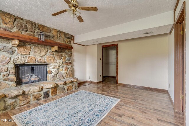 living room featuring light wood-type flooring, a textured ceiling, a stone fireplace, and ceiling fan