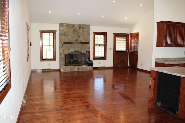 unfurnished living room with dark hardwood / wood-style floors, a stone fireplace, and plenty of natural light