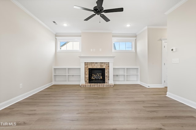 unfurnished living room with crown molding, a brick fireplace, ceiling fan, and light wood-type flooring