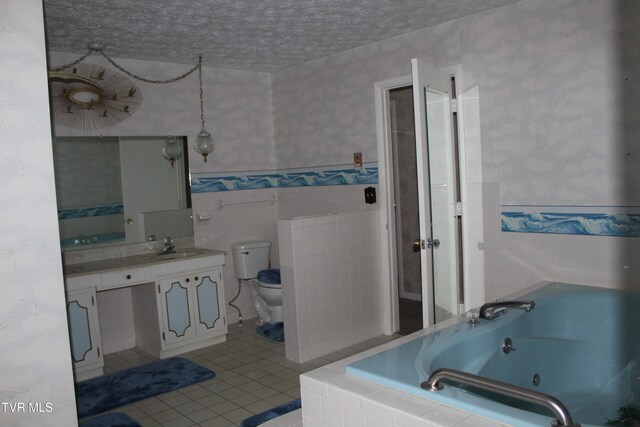 bathroom featuring a textured ceiling, tile patterned floors, a relaxing tiled tub, vanity, and toilet