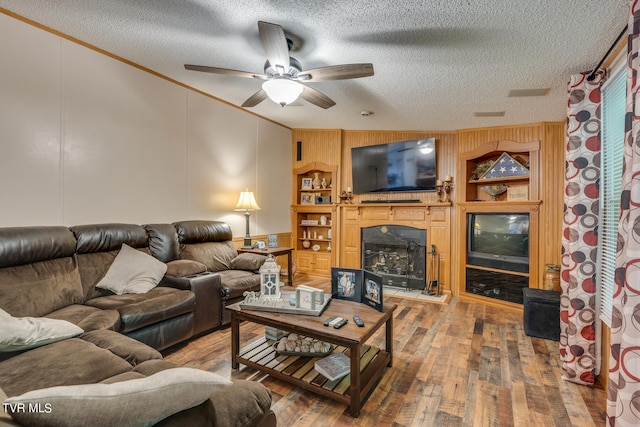 living room featuring wood-type flooring, a textured ceiling, ceiling fan, and crown molding